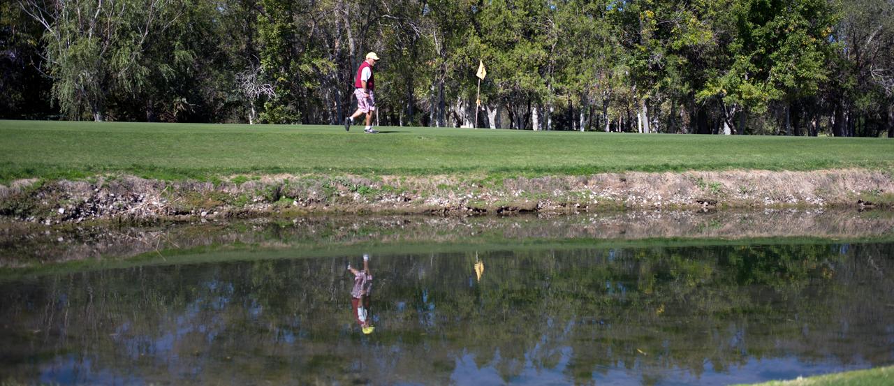 一名男子走向高尔夫球旗的英雄形象，前景是水的危险.